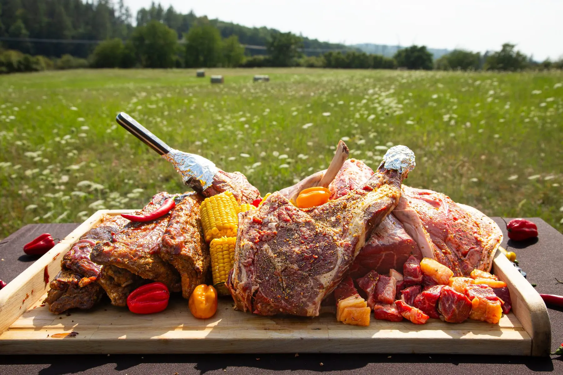 BBQ — prkno plné tomahawků, žeber a kukuřice na louce